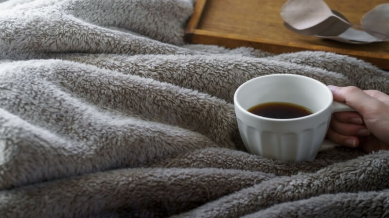グレーの毛布とコーヒーが入ったマグカップ