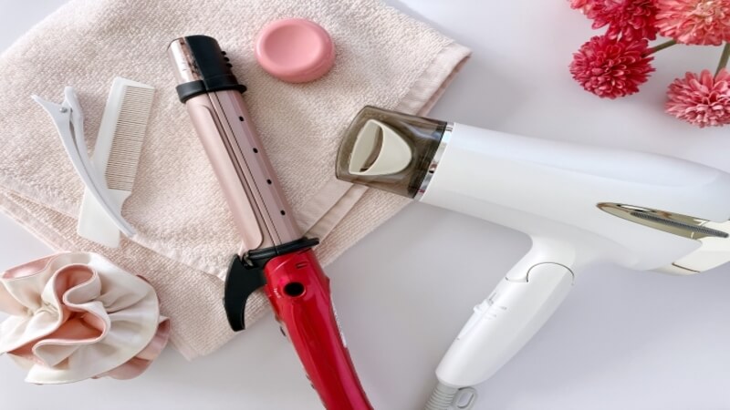 ドライヤー、ヘアアイロン、くし、ワックス、シュシュがタオルの上に置かれている