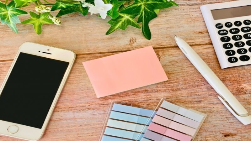 電卓、ペン、付箋とスマホが机に置かれている様子